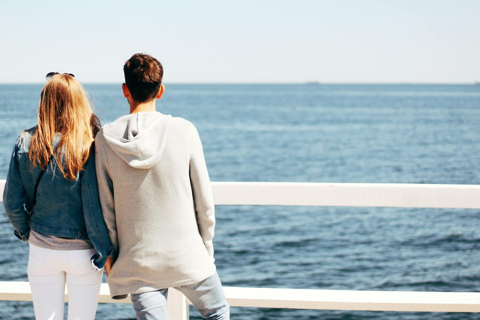man and woman beside wooden hand rail beside body of water