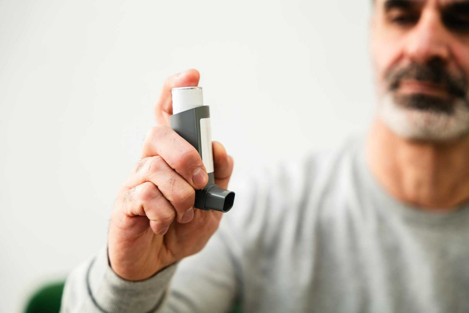 man using inhaler for respiratory health - Common Asthma Triggers