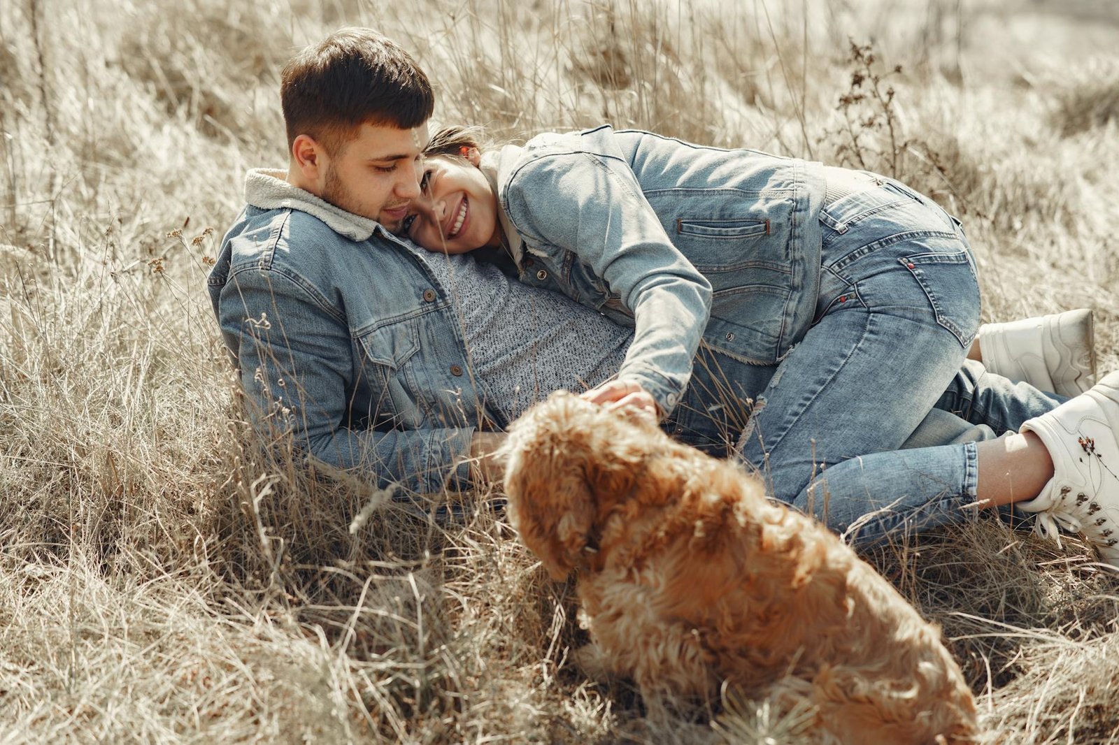 happy couple with dog lying on dry grass