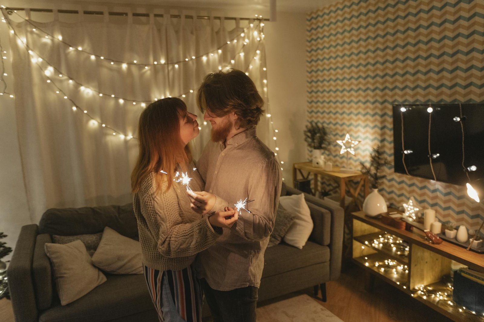 a man and a woman looking at each other while holding a burning sparkler at home