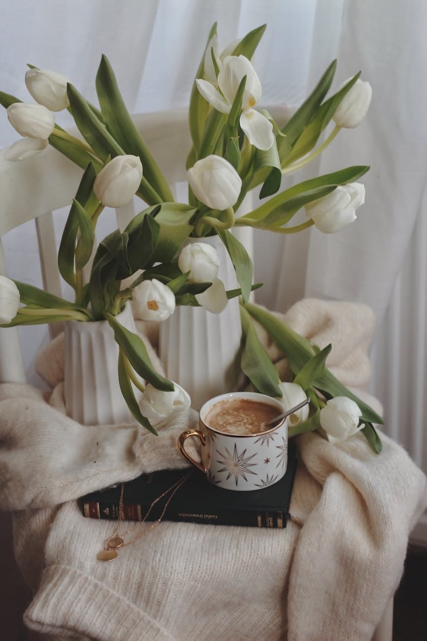 elegant composition of tulips bunches and cup of hot drink placed on knitted sweater