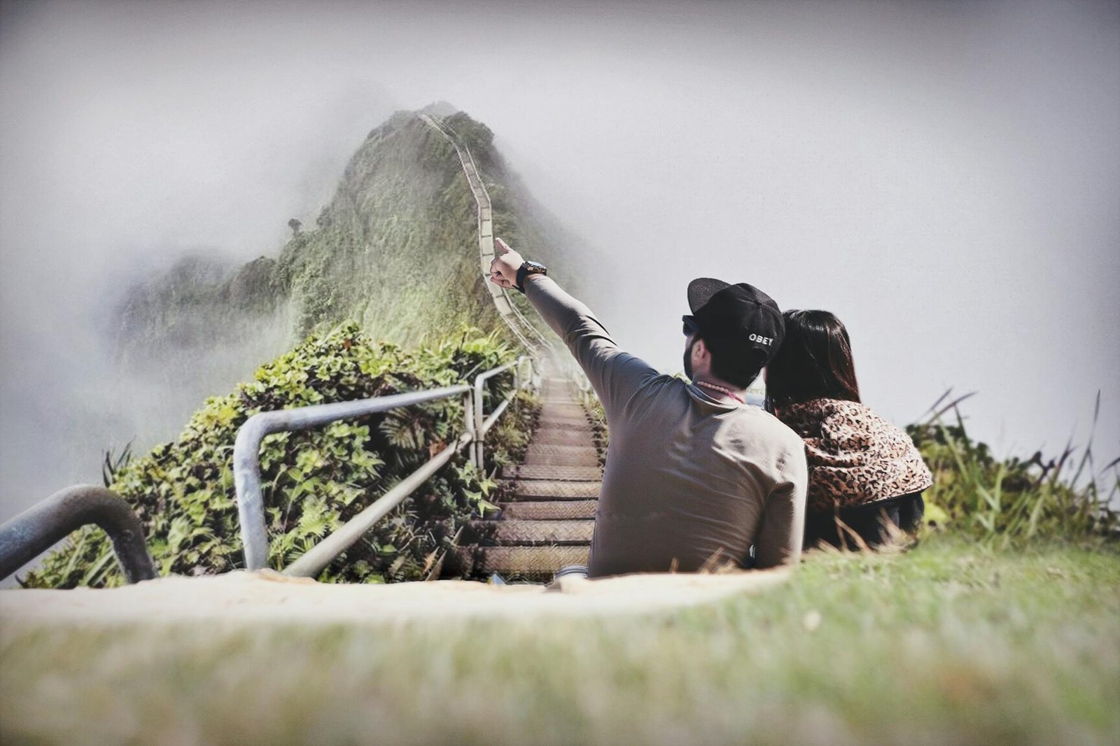 photography of couple sitting on green grass near bridge
